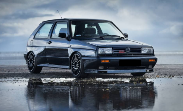 Foto de um Golf G60 Rallye preto estacionado em um terreno molhado.