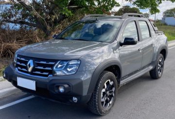 Foto de um Renault Oroch 2023 na cor cinza, estacionado em uma rua de asfalto. No fundo é possível ver uma árvore, grama e o céu azul.