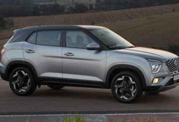 Foto de um Hyundai Creta G2 estacionado de lado em uma rua de asfalto. Atrás é possível ver uma pequena montanha com algumas árvores. O carro é prateado com o teto preto e tem rodas estilizadas.