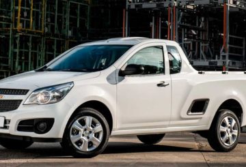 Foto da dianteira de um Chevrolet Montana G2 branco estacionado em uma rua de asfalto . Ao fundo é possível ver uma estrutura de ferros de uma construção.