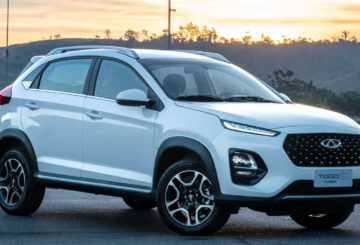 Foto de um Caoa Chery Tiggo 3X 2022 na cor branca. Na foto, o carro está parado em uma rua de asfalto e, ao fundo, é possível ver a silhueta de árvores e o pôr-do-sol.