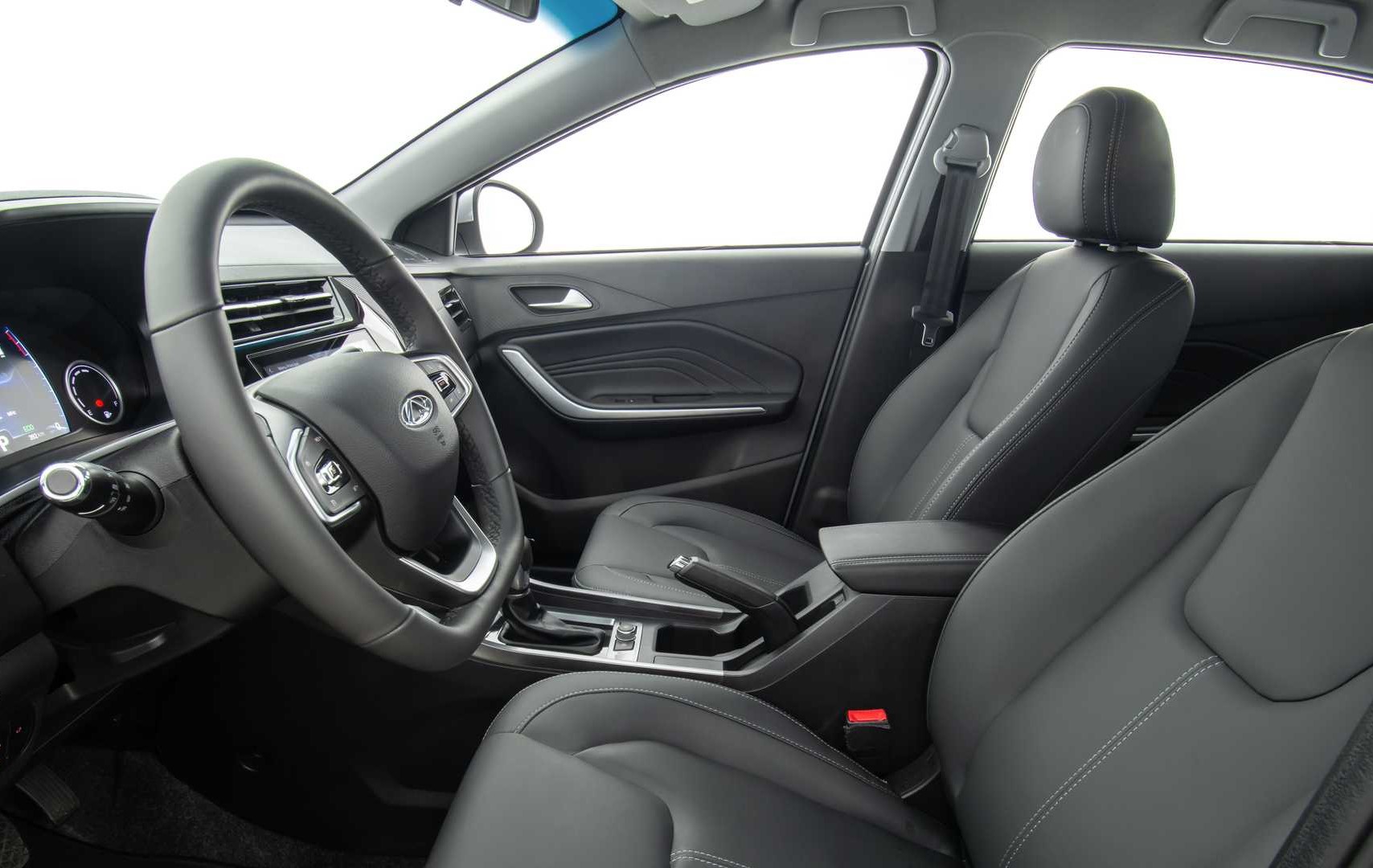 Foto do interior do carro mostrando a lateral do volante, a parte interna da porta do passageiro, a lateral do câmbio e os bancos dianteiros. O ambiente é predominantemente preto com detalhes prateados. As costuras do banco são em cinza claro.