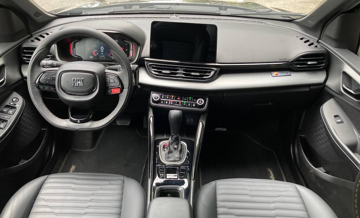 Foto mostrando o painel, o volante, o câmbio, os controles e saídas de ar , os detalhes do interior e os assentos dos bancos dianteiros do carro.