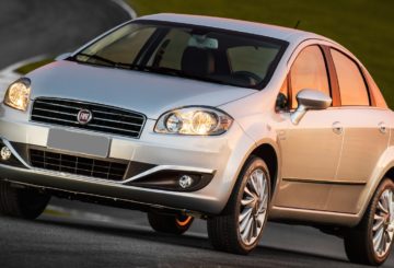 Foto mostrando a dianteira de um Fiat Linea prateado que está sendo dirigido em uma rua de asfalto.