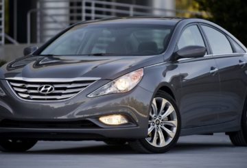 Foto mostrando a dianteira de um Hyundai Sonata G6 cinza estacionado em uma rua de asfalto.