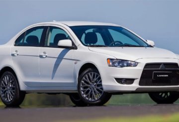 Foto mostrando a dianteira de um Mitsubishi Lancer sedan branco que está estacionado em uma rua de asfalto.