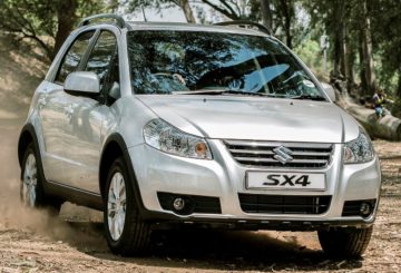 Foto mostrando a dianteira de um Suzuki SX4 prateado que está sendo dirigido em uma estrada de terra.