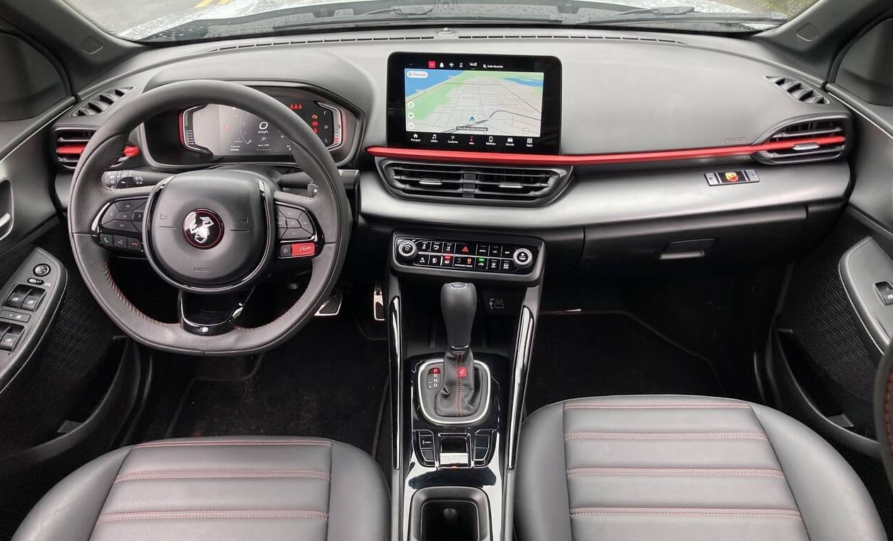 Foto ampla mostrando a parte interior do carro. Nela, é possível ver o volante, o painel, a central multimídia, o câmbio, uma parte da lateral das portas e os assentos dos bancos dianteiros.
