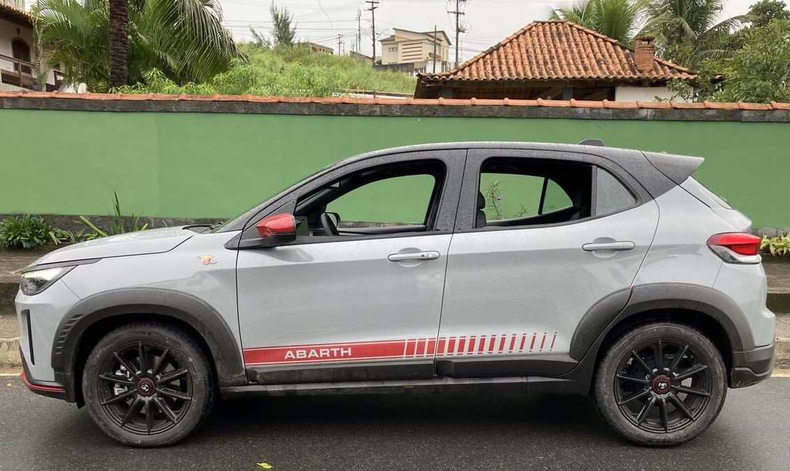 Foto mostrando a lateral esquerda de um Fiat Pulse Abarth 2023 cinza claro com detalhes em vermelho e rodas pretas.
