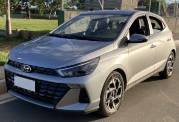 Foto mostrando a diagonal esquerda de um Hyundai HB20 2023 prateado estacionado em uma estrada de asfato.