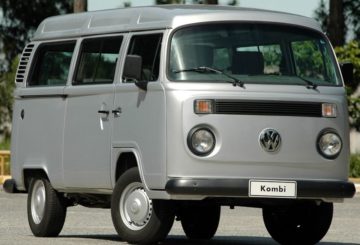Foto mostrando a dianteira de um Volkswagen Kombi prateado estacionado em uma rua de asfalto.