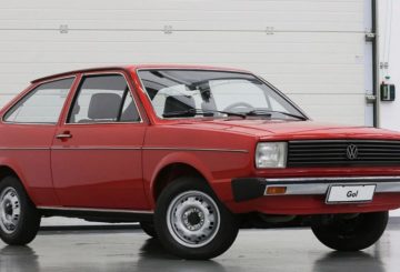 Foto mostrando a dianteira de um Volkswagen Gol G1 vermelho estacionado em frente a um portão branco