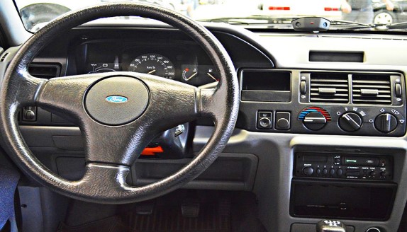 Foto de detalhe mostrando o painel do carro. É possível ver o volante, os comandos e as saídas de ar, o rádio e o velocímetro.