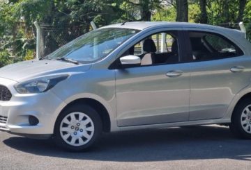 Foto mostrando a lateral direita de um Ford Ka SE 2015 prateado estacionado em uma rua de asfalto.
