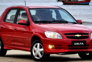 Foto mostrando a diagonal direita de um Chevrolet Celta 2012 LT vermelho estacionado em uma rua de asfalto.