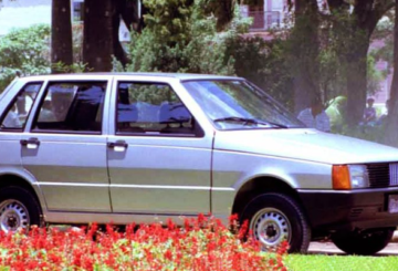 Foto mostrando a diagonal direita de um Fiat Uno Mille Eletronic 1994 prateado estacionado na grama.