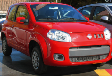 Foto mostrando a dianteira de um Fiat Uno Vivace 2014 vermelho que está parado em um estacionamento.