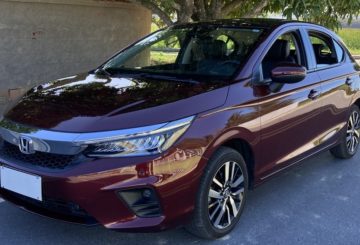 Foto mostrando a diagonal esquerda de um Honda City Hatchback Vermelho Mercúrio estacionado em uma rua de asfalto.