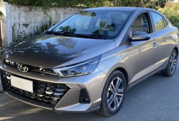 Foto mostrando a diagonal esquerda de um Hyundai HB20S 2023 cinza estacionado em uma rua de asfalto.