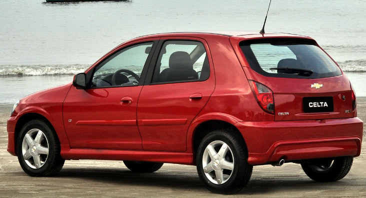 Foto mostrando a traseira de um Chevrolet Celta LT 2012 vermelho estacionado em uma praia.
