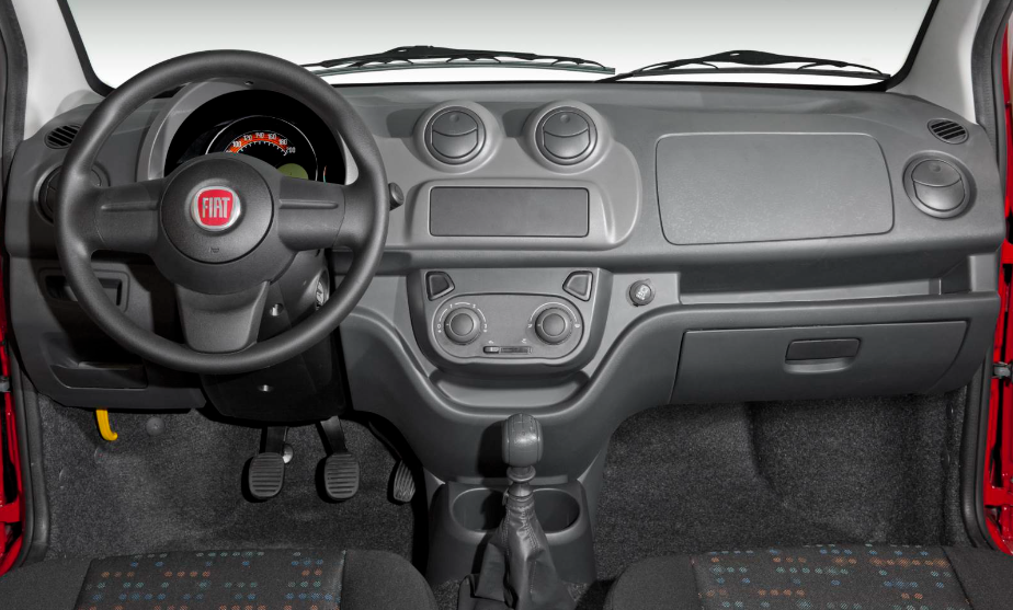 Foto mostrando a cabine do carro. É possível ver o volante, o painel, as saídas e os controles de ar, o câmbio e os assentos dos bancos dianteiros.