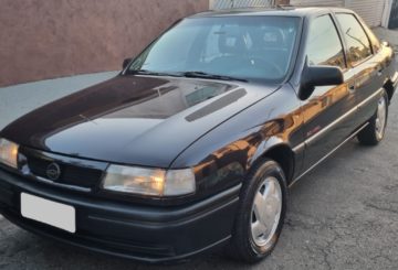 Foto mostrando a dianteira de um Chevrolet Vectra G1 preto estacionado em uma rua de asfalto.