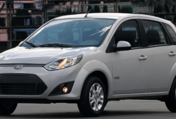 Foto mostrando a dianteira de um Ford Fiesta 2014 prateado estacionado em uma rua de asfalto.