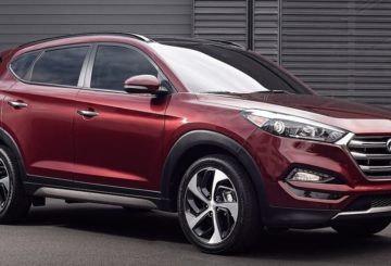 Foto mostrando a diagonal direita de um Hyundai Tucson G3 vermelho estacionado em uma rua de asfalto.