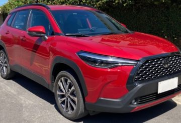 Foto mostrando a diagonal direita de um Toyota Corolla Cross 2024 vermelho estacionado em uma rua de asfalto.