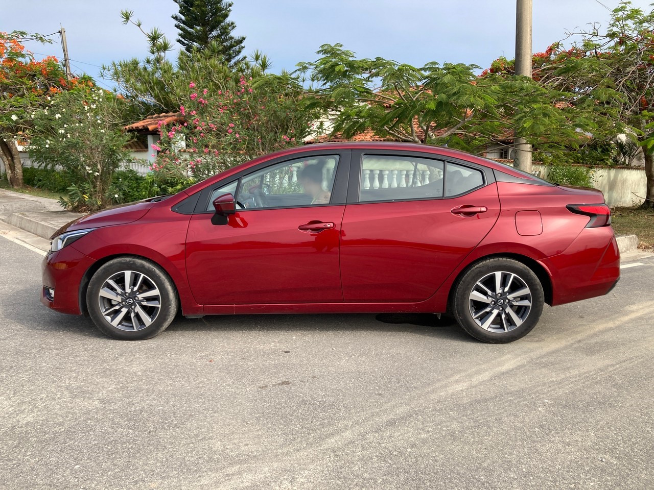 A imagem mostra a lateral do Nissan Versa Advance 2024 de cor vermelha.