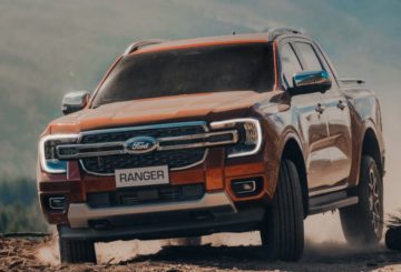 A imagem mostra a Ford Ranger XLS 2024, com pintura na cor laranja, andando sobre uma estrada de terra.