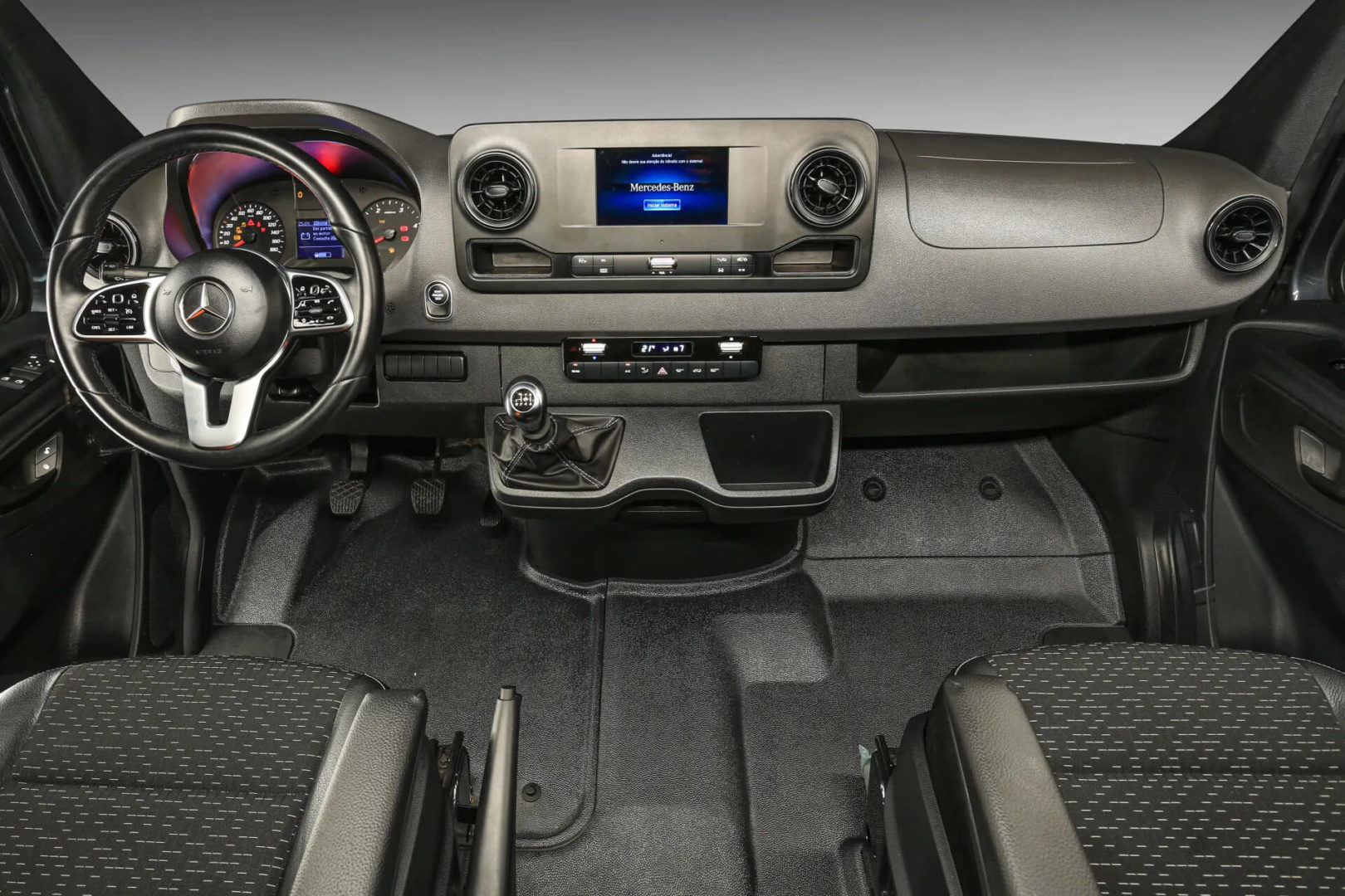 Foto interna do Mercedes-Benz Sprinter 517 Vidrado, exibindo o painel de instrumentos, volante multifuncional, central multimídia, parte dos bancos e portas. 