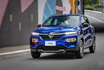 Foto do Renault Kwid 2024 de frente, andando na rua, exibindo a dianteira e parcialmente a lateral do motorista.