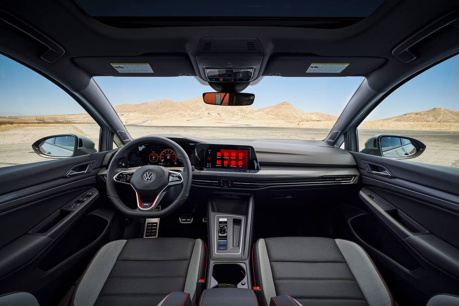 Foto interna do Volkswagen Golf GTI 2023, exibindo o painel de instrumentos, volante multifuncional, central multimídia e parte dos bancos e portas.