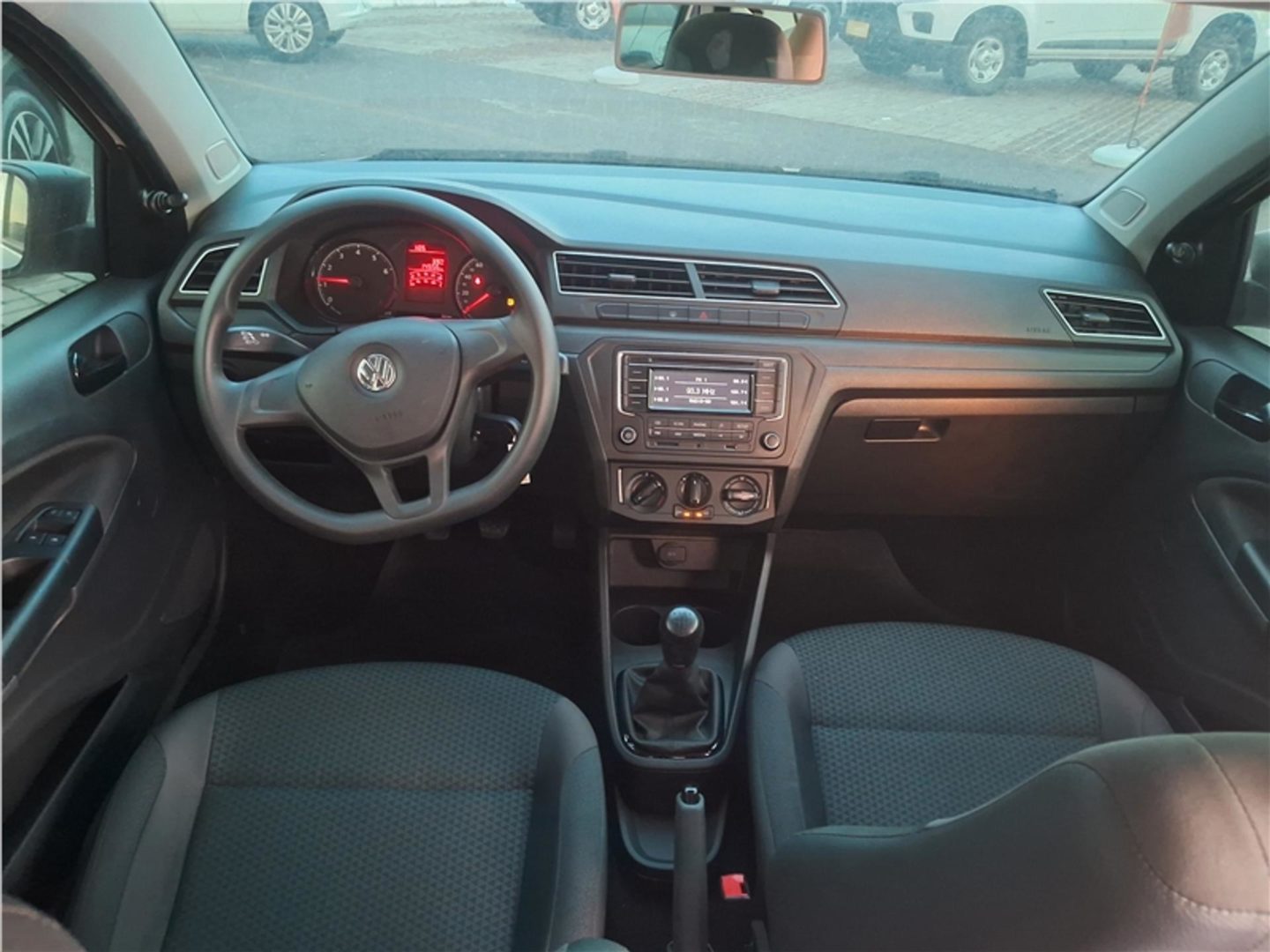 Foto interior do Volkswagen Voyage 2023, exibindo o volante, painel de instrumentos, central multimídia, parte dos bancos e portas.
