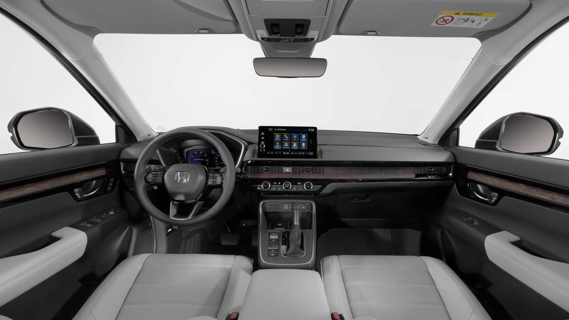 Foto interna do Honda CR-V Advanced Hybrid 2024, exibindo o painel de instrumentos, volante multifuncional, central multimídia, parte dos bancos e portas.
