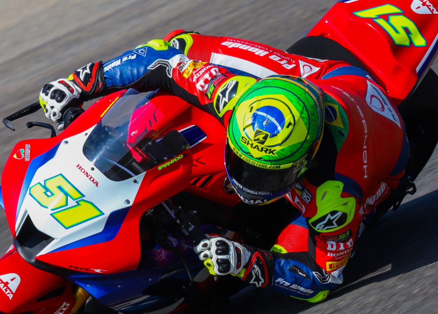 Esta foto mostra Granado em pilotando sua moto da Honda. O veículo tem pintura predominantemente vermelha, com detalhes em azul e branco. O piloto está utilizando um macacação nas mesmas cores e capacete verde, amarelo e azul.