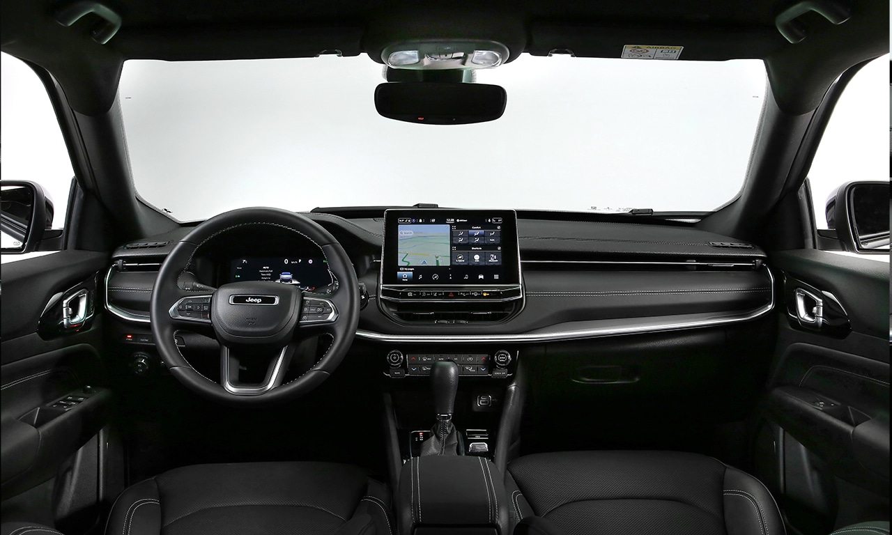 Foto interna do Jeep Compass Sport 2024, exibindo o painel de instrumentos, volante multifuncional, central multimídia, parte dos bancos e portas.