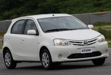 A foto mostra um Toyota Etios com pintura na cor branca. Ele está em movimento em um local asfaltado.