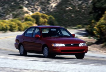 Foto frontal do Toyota Corolla LE 1.8 (1993-1998) na estrada, exibindo a frente e a lateral do modelo.