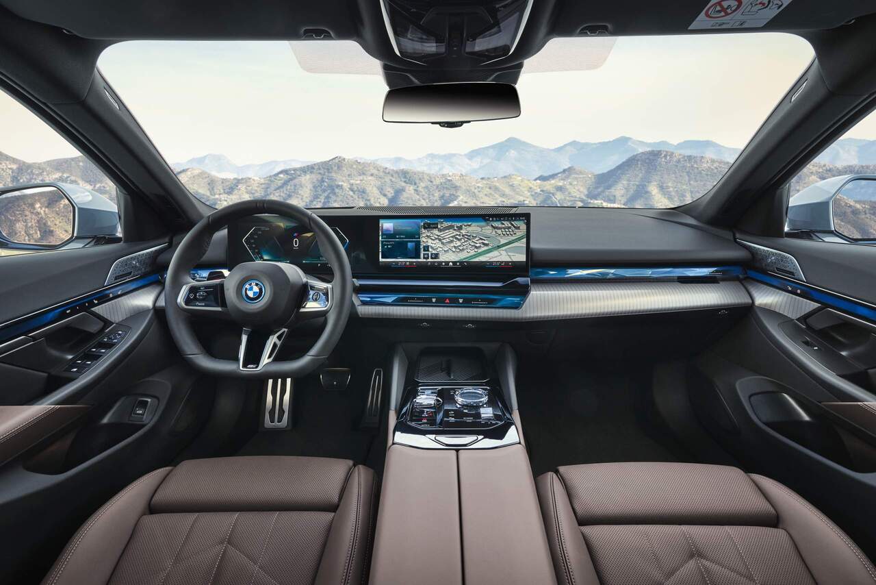 Foto interna do BMW 520i 2024 , exibindo o painel e central multimídia digitais, parte dos bancos, portas e console central.