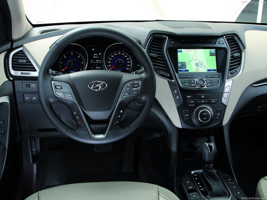 Foto interna do Hyundai Santa Fe G3, exibindo o painel de instrumentos, volante multifuncional., central multimídia e parte do console central.