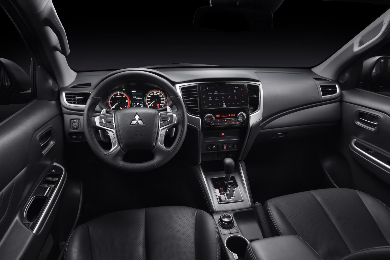 Foto interna da Mitsubishi L200 Triton Sport HPE-S 2.4 (2018-atual), exibindo o painel de instrumentos, volante multifuncional, central multimídia e parte dos bancos.