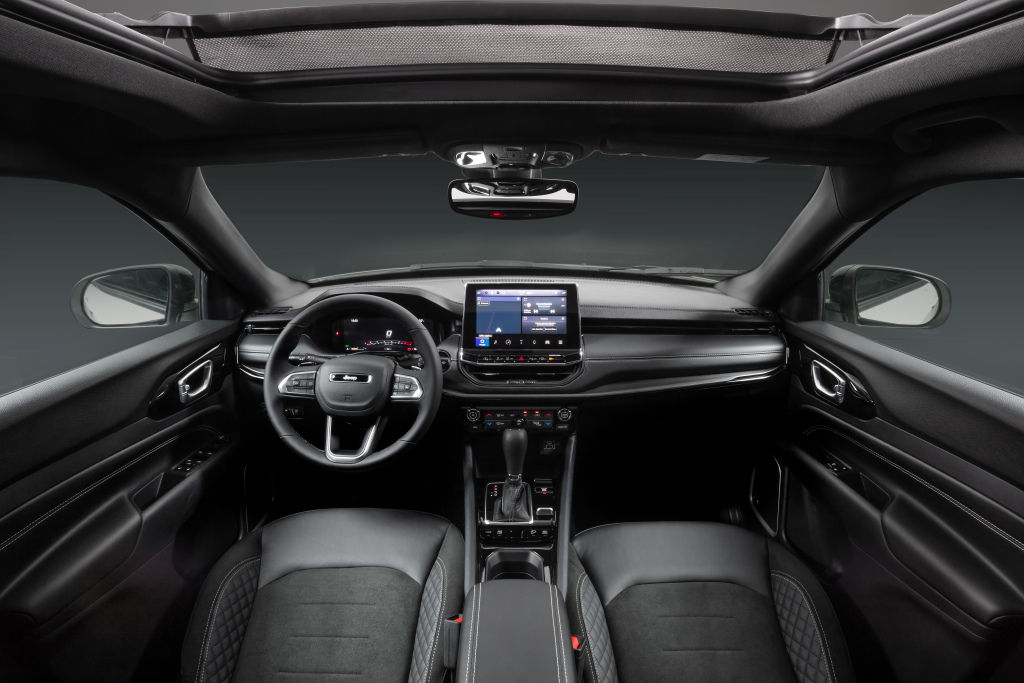 Foto interna do Jeep Compass Limited TD350 2025, exibindo o painel de instrumentos digital, volante multifuncional, central multimídia, parte dos bancos e das portas. 