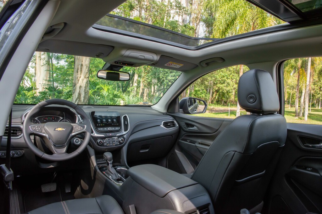 Foto interna do Chevrolet Equinox Premier 2024, exibindo o painel de instrumentos, volante multifuncional, central multimídia, parte dos bancos e das portas.