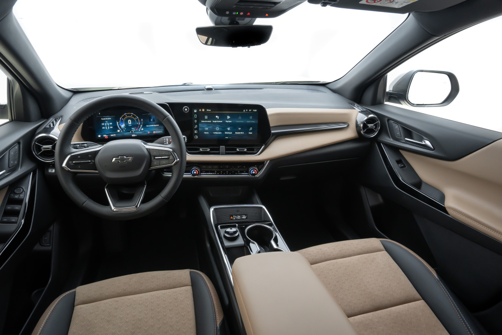 Foto interna do Chevrolet Equinox Activ 2025, exibindo o painel de instrumentos digital, volante multifuncional, central multimídia, parte dos bancos e das portas.