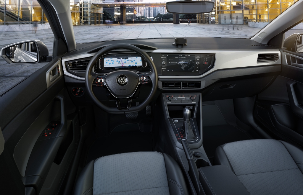 Foto interna do Volkswagen Virtus Comfortline 2025, exibindo o painel de instrumentos digital, volante multifuncional, central multimídia, parte dos bancos e das portas.