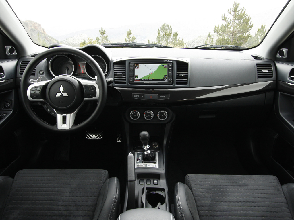 Foto interna do Mitsubishi Lancer Evolution X (2010-2015), exibindo o painel de instrumentos, volante multifuncional, central multimídia e parte dos bancos.