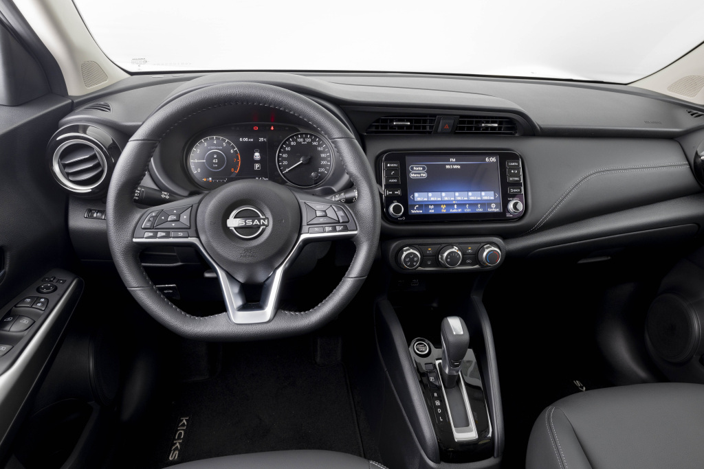 Foto interna do Nissan Kicks Play Sense 2025, exibindo o painel de instrumentos, volante multifuncional, central multimídia, parte dos bancos e das portas.